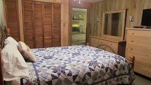 Quarto com cama, guarda-roupa de madeira, penteadeira e televisão.
