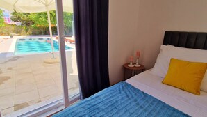 Een slaapkamer met een bed, nachtkastje en uitzicht op een buitenzwembad.