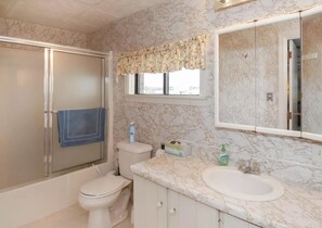 Une salle de bain avec un pare-baignoire en marbre, un grand miroir, des toilettes et une cabine de douche.