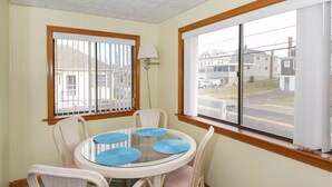 Un coin repas avec une table ronde en verre, des chaises en osier blanches et des sets de table bleus.