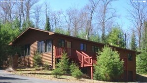 A two-story wooden cabin with a red staircase, surrounded by trees.