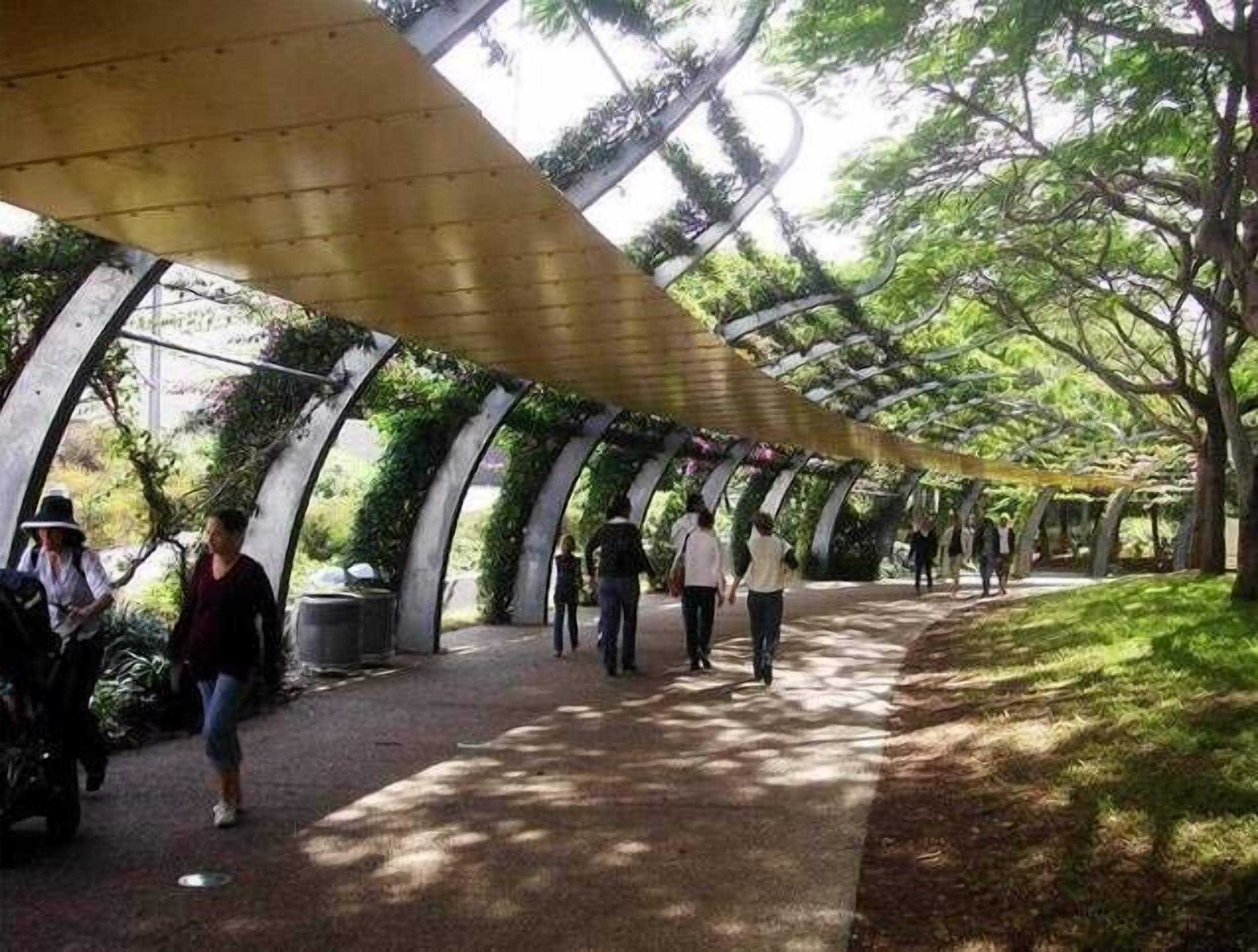 A covered walkway with a curved roof, surrounded by trees and greenery.