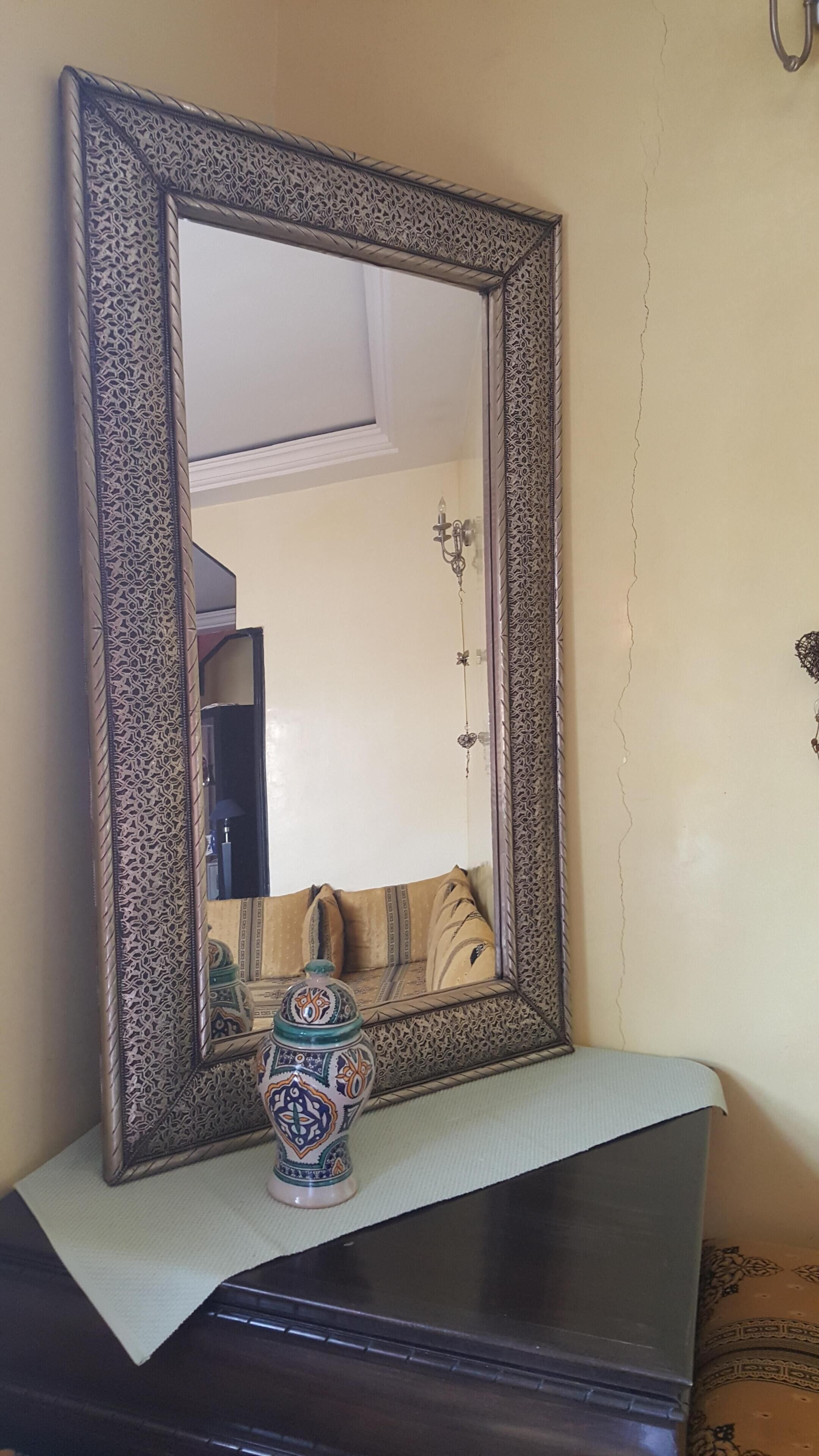 Un miroir doté d’un cadre orné, posé sur une surface sombre.