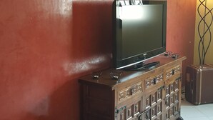 A living room with a flat-screen TV on a wooden cabinet, a red wall, and a tiled floor. - A Cozy Flat In A Quite Neighborhood (Fès)