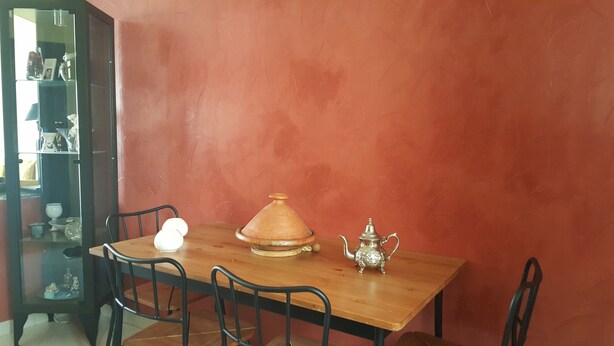A dining area with a wooden table, four chairs, a Moroccan tagine, and a teapot. - A Cozy Flat In A Quite Neighborhood (Fès)