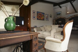 A living room with a wooden desk, a green vase, a white armchair, and a fireplace.