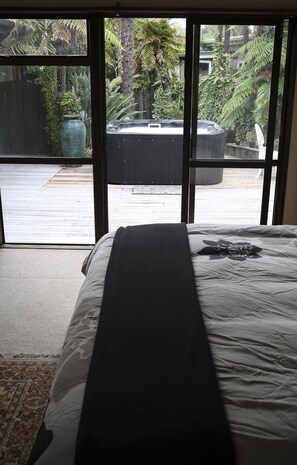 A bedroom with a large bed, a view of a hot tub, and a wooden deck outside.