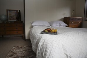 A neatly made bed with a white quilt, a bedside table with a lamp, and a tray of fruit and juice on the bed.