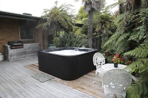 A hot tub on a wooden deck with a brick wall and a window in the background. - Rose Lake Retreat - Spa Pool, Lake Views, Sleeps 8 (Rotorua)