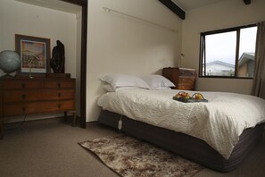 A bedroom with a bed, a dresser, a globe, a framed picture, and a window with a view. - Rose Lake Retreat - Spa Pool, Lake Views, Sleeps 8 (Rotorua)