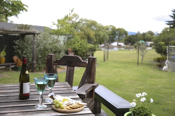 A wooden table with a bottle of wine, two glasses, a plate with grapes and crackers, and a potted plant.