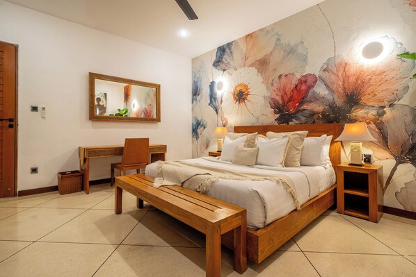 A bedroom with a bed, a desk, a chair, a bench, and a large floral wall mural.
