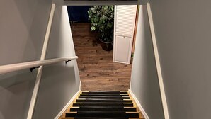 Eine Treppe mit einem 'WELCOME'-Schild oben, das zu einem Raum mit Holzboden und einer Pflanze im Hintergrund führt.