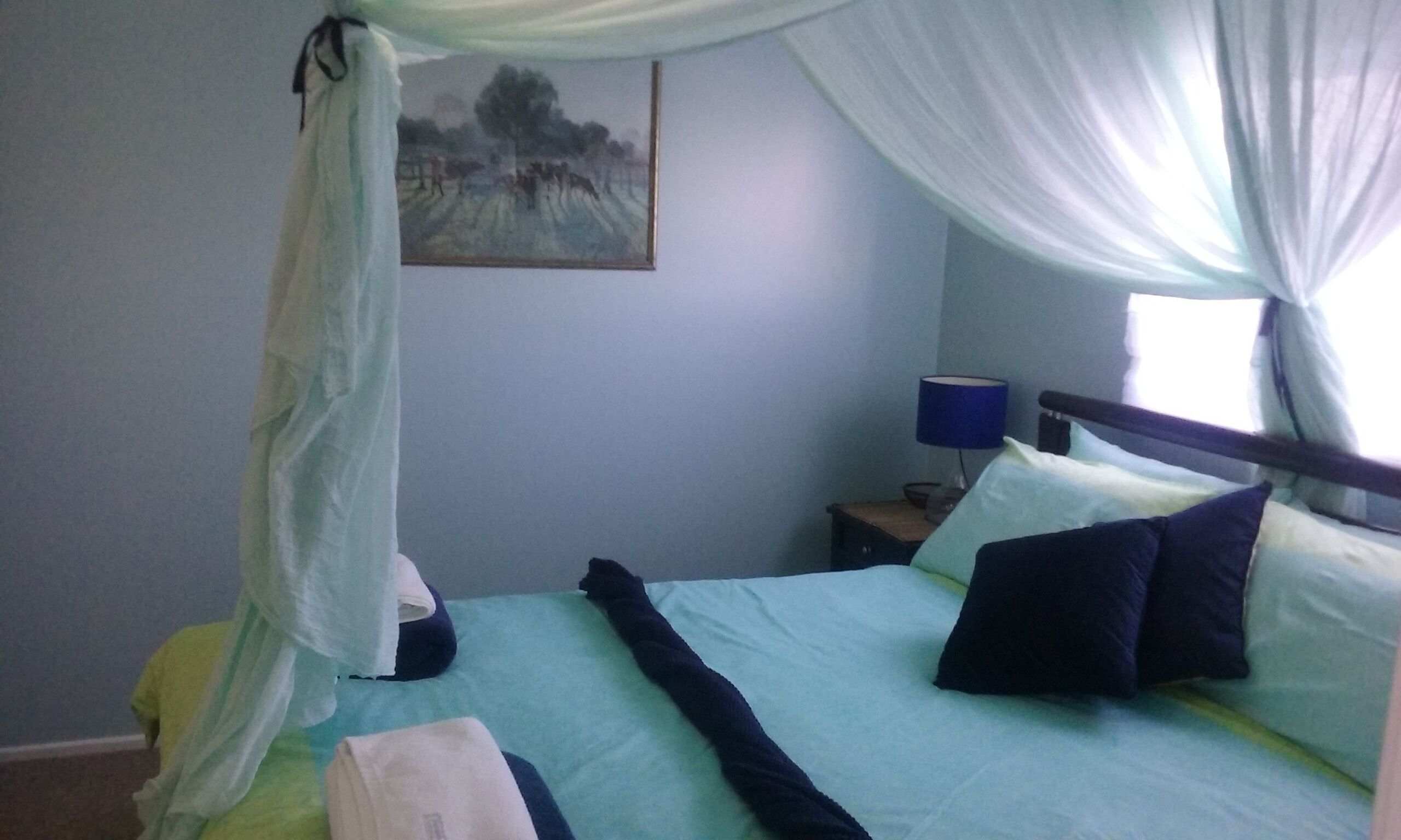 A bedroom with a bed, a nightstand, a lamp, and a painting on the wall.
