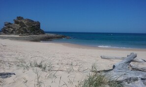 A beach with clear blue water, sandy shore, and a large rock formation. - Oceanview 6 at Nambucca with rooftop tce & spa (Nambucca Heads)