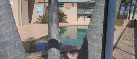 A pool area with a clear view of the pool, surrounded by palm trees and a building with a sign indicating a fire exit.