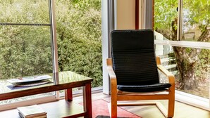 Une pièce avec une grande fenêtre, une chaise en bois et une petite table sur laquelle sont posés des livres.