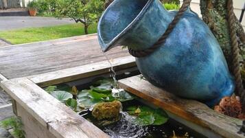 A metal bucket pouring water into a pond with lily pads and a mossy rock.