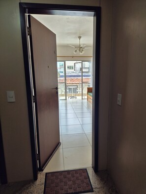 A hallway leading to a balcony with a ceiling fan and a view of a tiled roof.
