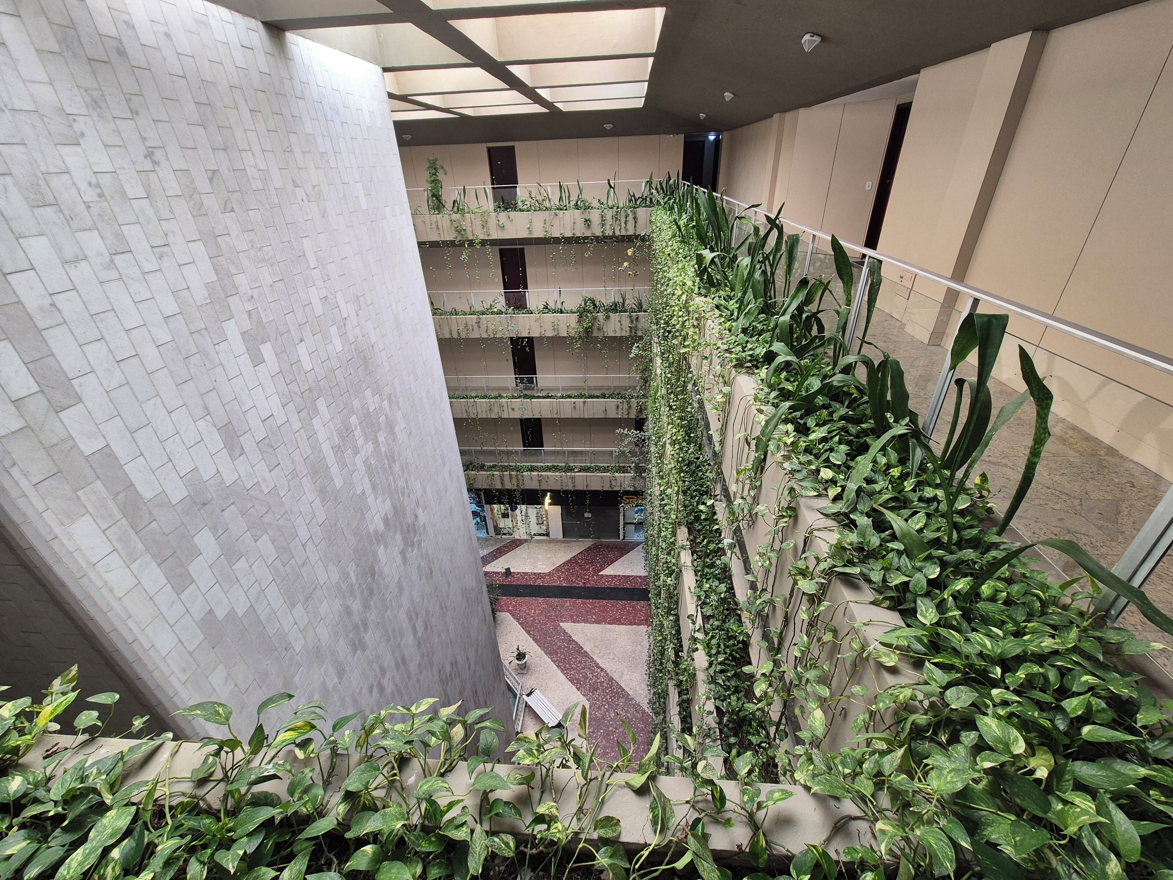 A multi-level atrium with a brick-patterned wall, a central open space, and a variety of potted plants.