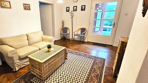 A living room with a beige sofa, a wooden coffee table with a plant, and a patterned rug. There are two chairs, a coat rack, and a door with a window. - Amazing house with beautiful garden, 5 bedrooms, terrace, in the City Centre (Sibiu)