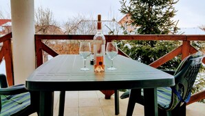 A table with a bottle and two glasses on a patio with wooden railings and a view of trees and buildings. - Amazing house with beautiful garden, 5 bedrooms, terrace, in the City Centre (Sibiu)