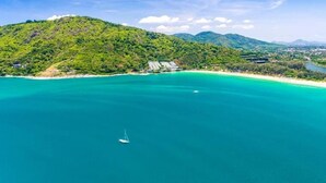 Eine Küstenlandschaft mit klarem türkisblauem Meer, einem kleinen Segelboot und einer hügeligen Kulisse.