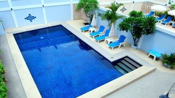 Ein rechteckiger Pool mit blauem Wasser, umgeben von Liegestühlen, kleinen Tischen und Topfpflanzen.
