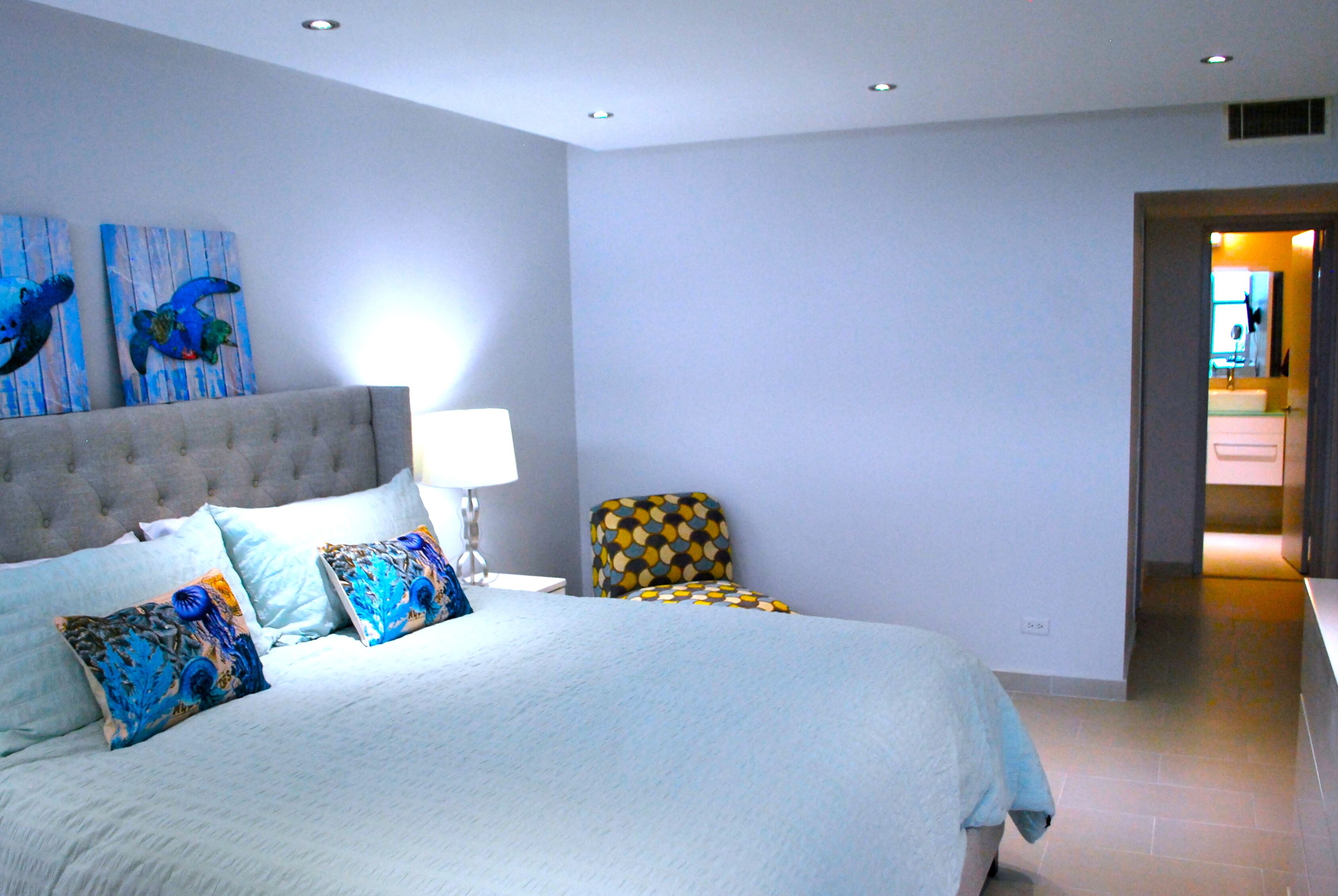 Une chambre à coucher avec un grand lit, une table de chevet, une lampe et deux œuvres d’art murales.
