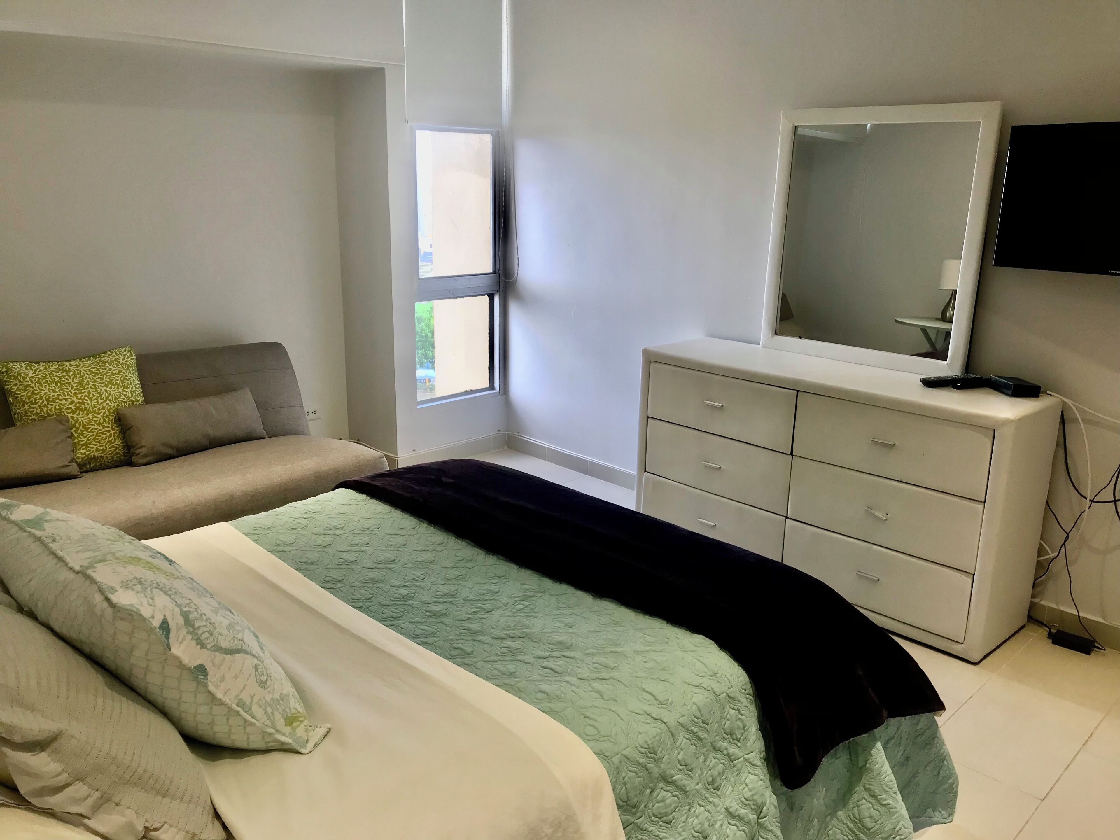 A bedroom with a bed, a dresser, a mirror, and a window.