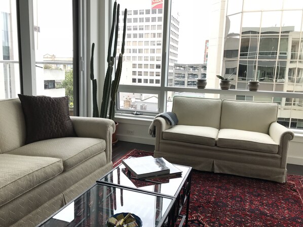 Ein modernes Wohnzimmer mit einem beigefarbenen Sofa, einem Glastisch und einem roten Teppich mit Muster.