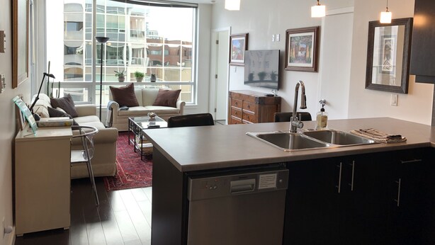 A modern kitchen with a central island, stainless steel appliances, and a large window offering a city view. - Bright and airy 2bed/2bath condo in the heart of downtown Victoria (Victoria)