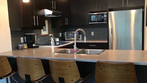 A modern kitchen with dark cabinetry, stainless steel appliances, and a central island with bar stools. - Bright and airy 2bed/2bath condo in the heart of downtown Victoria (Victoria)