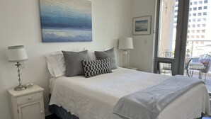 A bedroom with a bed, two bedside tables, a lamp, a painting, and a view of the outside. - Bright and airy 2bed/2bath condo in the heart of downtown Victoria (Victoria)