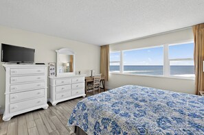 Quarto com cama grande, cômoda, escrivaninha, televisão e vista para o oceano.