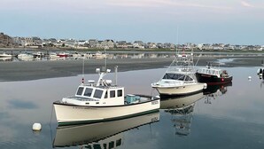 Two boats docked at a marina with a calm water surface reflecting the boats and a residential area in the background. - Beachy Condo! Cozy studio 3 minutes to Wells Beach (Wells)