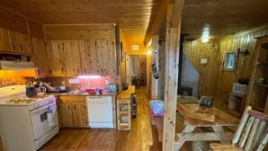 Interior d'una cabana de fusta amb cuina, zona de menjador i una escala que puja a un altell.