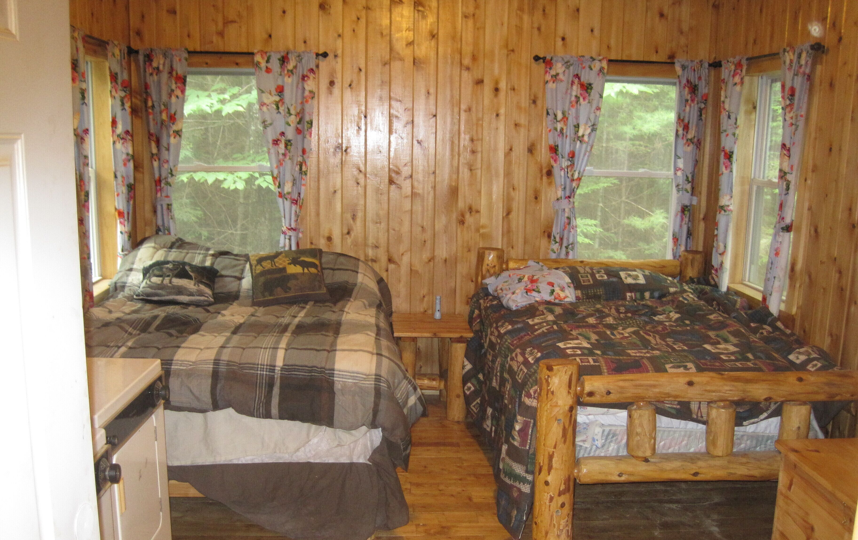 A cabin with two wooden beds, a small table, and a window with floral curtains.