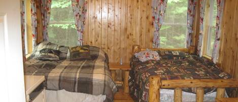 A cabin with two wooden beds, a small table, and a window with floral curtains.