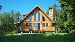 Una cabaña de troncos con chimenea de piedra, ventanas grandes y un porche.