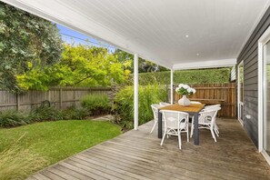 Eine überdachte Terrasse mit Holzdeck, weißen Korbmöbeln und einem Tisch mit Blumen.