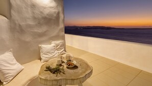 A balcony with a view of the sea at sunset, a round wooden table with a bowl of snacks, and a white cushioned bench. - Private pool, Breathtaking Panoramic View to the Sea & Sunset (Paros)