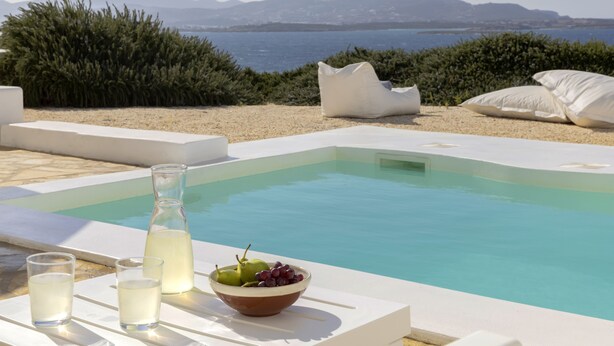 A pool area with a clear view of the sea and mountains, a bowl of fruit, and a bottle of drink. - Private pool, Breathtaking Panoramic View to the Sea & Sunset (Paros)