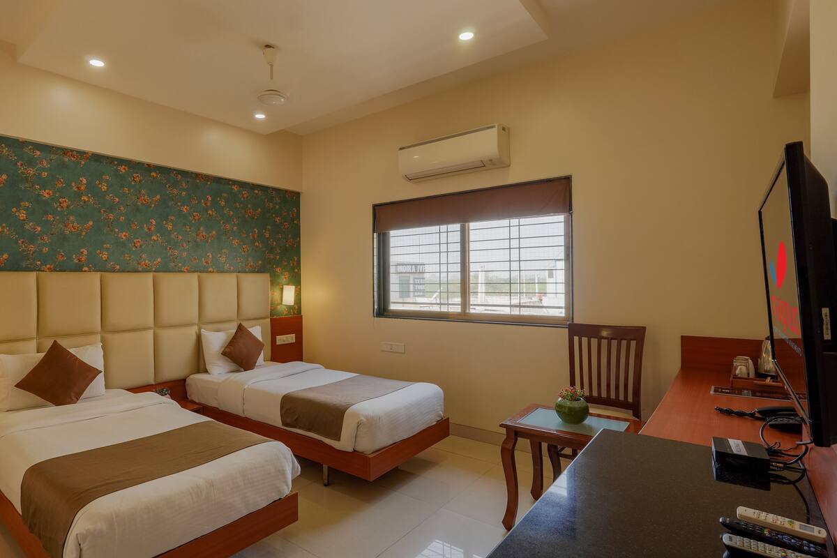 A hotel room with two beds, a desk, a chair, a TV, and an air conditioning unit.