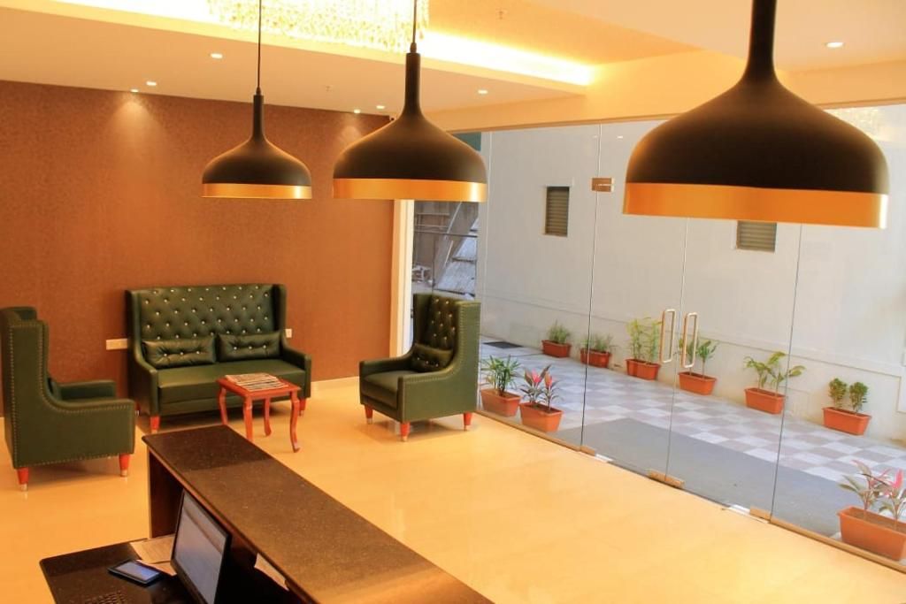 A reception area with a reception desk, two green armchairs, a small table, and a large window with potted plants.