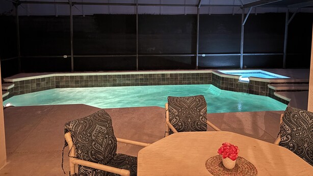 A covered outdoor swimming pool with a hot tub, surrounded by chairs and a table.