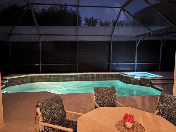 A covered outdoor swimming pool with a hot tub, surrounded by chairs and a table.