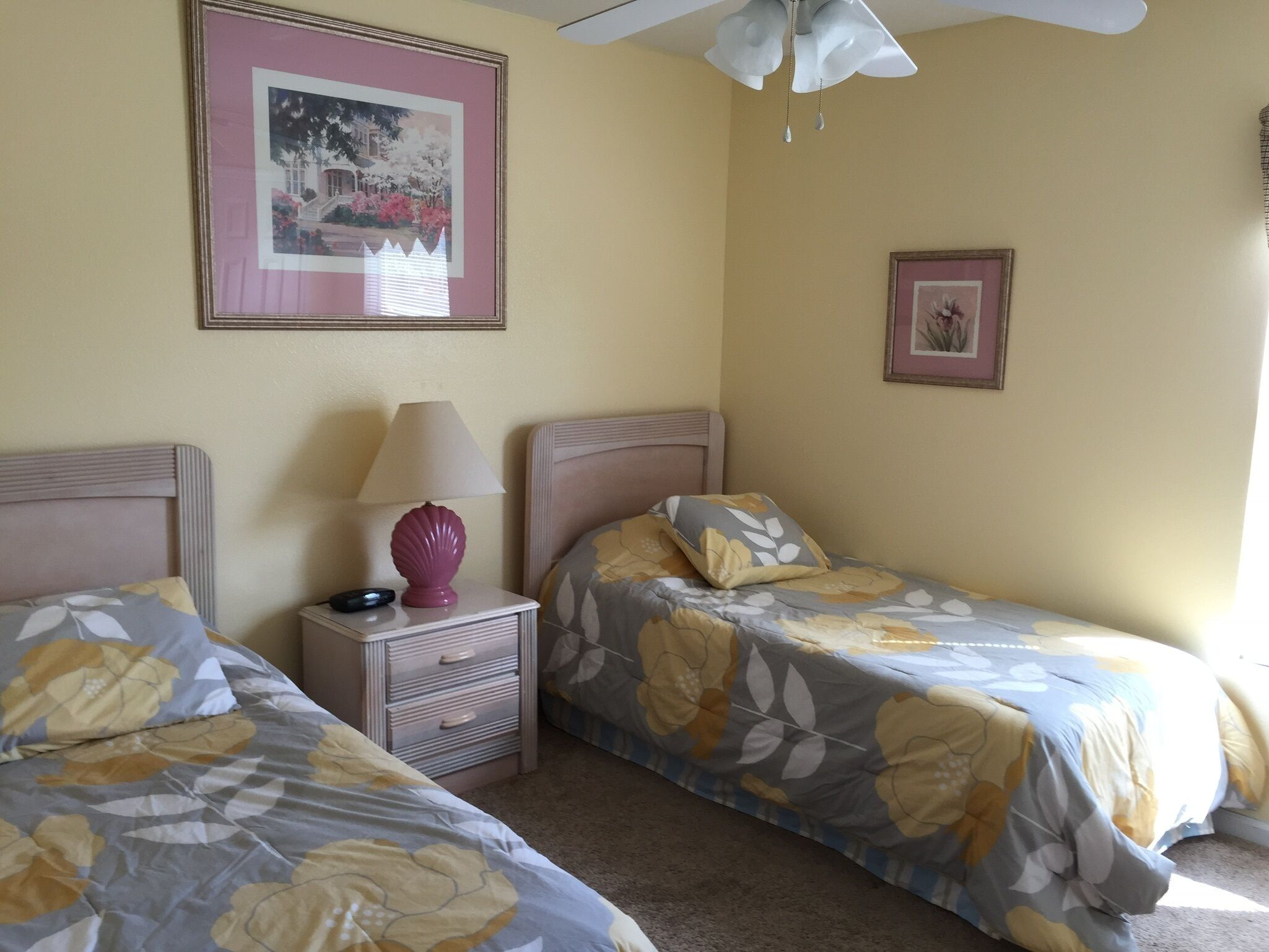 Ein Schlafzimmer mit zwei Betten, einem Nachttisch, einer Lampe und zwei gerahmten Bildern an der Wand.