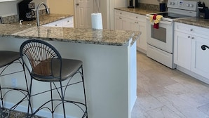 A kitchen with white cabinets, a granite countertop, a refrigerator, a microwave, an oven, and a sink.