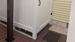 Un contenedor de almacenamiento exterior blanco con un asa, una ventana y una puerta, junto a una casa con revestimiento color beige y una ventana.